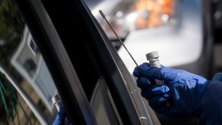 A public health nurse with Contra Costa Health Services wearing personal protective equipment holds a Covid-19 test swab at a testing site in Concor