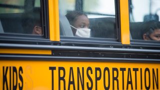 A student wearing a face mask peers out of a school bus window.