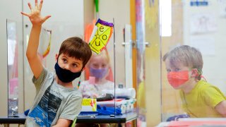 kindergarten students wear masks and are separated by plexiglass during a math lesson