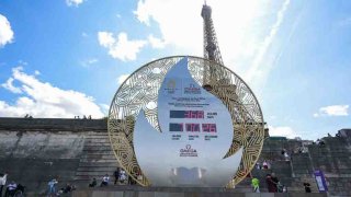 Los peatones pasan frente a un tablero que muestra la cuenta regresiva para el inicio de los Juegos Olímpicos de París 2024 frente a la Torre Eiffel en París, el 26 de julio de 2023.