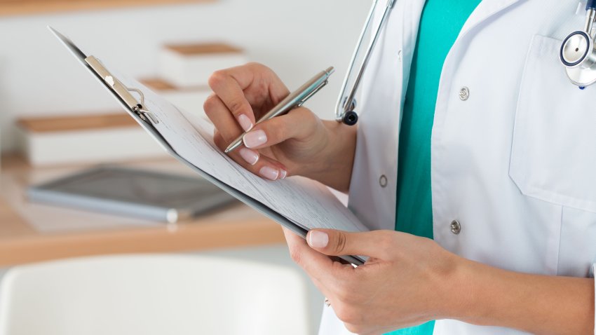 Close-up view of female doctor hands filling patient registration form. Healthcare and medical concept