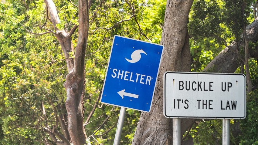 Hurricane evacuation shelter blue sign on road and seat belt buckle up it’s the law text with arrow direction in Naples, Florida during day