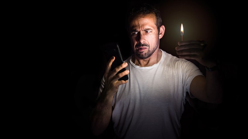 Man looking at his cell phone with a match in the dark. Blackout concept. Selective focus.