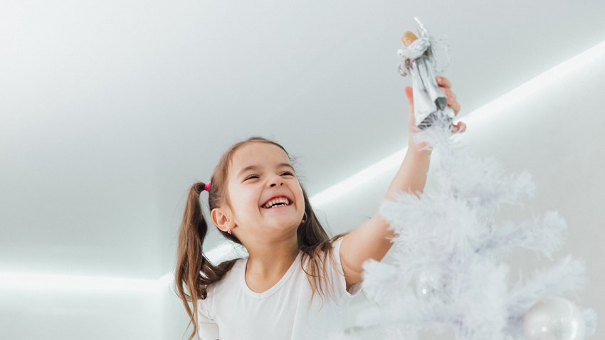 Laughing girl putting silver angel on Christmas tree