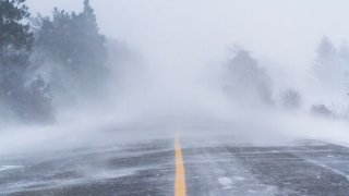 Una fuerte ventisca cubre de nieve una franja de carretera.