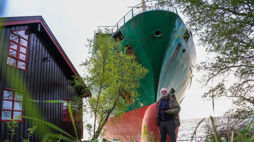 Johan Helberg poses next to his house and a 135-meter-long container ship by the shore in the Trondheimsfjord outside Byneset by Trondheim, Norway, on May 22, 2025, after the ship ran aground almost hitting his house. (Photo by Jan Langhaug / NTB / AFP) / Norway OUT (Photo by JAN LANGHAUG/NTB/AFP via Getty Images)