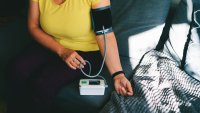 A close-up image of a person checking their blood pressure at home using a digital blood pressure monitor. The scene shows a relaxed individual seated on a cozy couch with a blood pressure cuff on their arm, illustrating the ease and convenience of home health monitoring. This image is ideal for conveying themes of health awareness, self-care, or medical technology in everyday life.